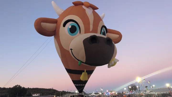 The cow-shaped balloon faces the crowd above the field.