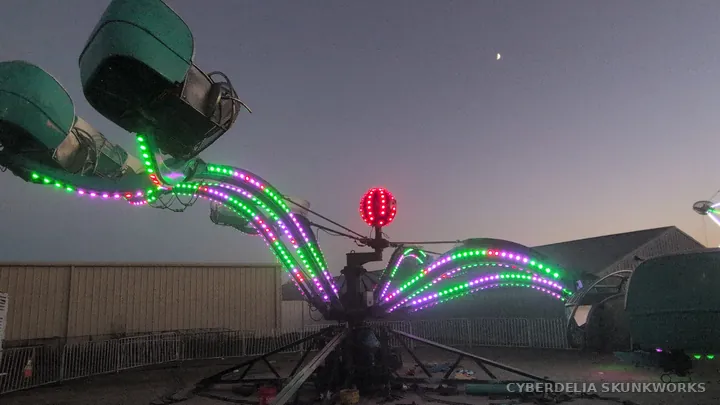 Green lights trace a ride beside a festival tent.
