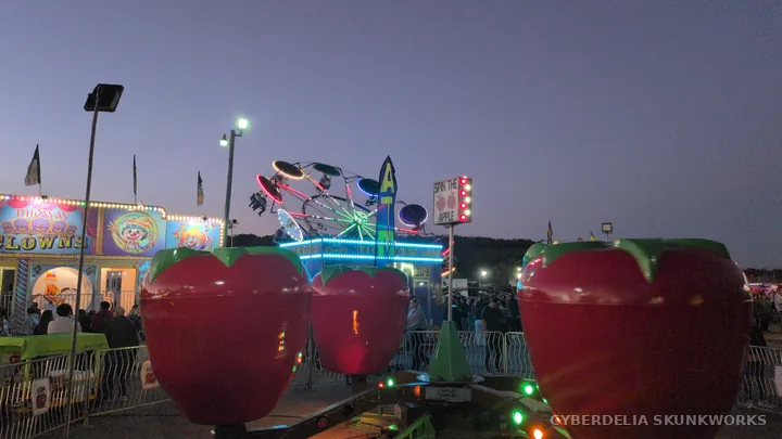 Strawberry-shaped cars and midway lights at dusk.