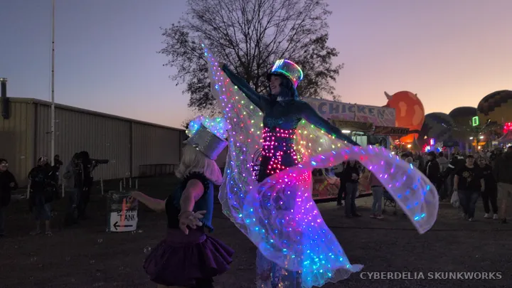 The LED-winged performer turns beside her companion.