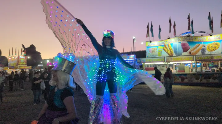 An Inspyral Circus performer opens illuminated wings against the evening sky.