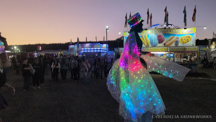 A lit costume stands out against spectators and food stands.