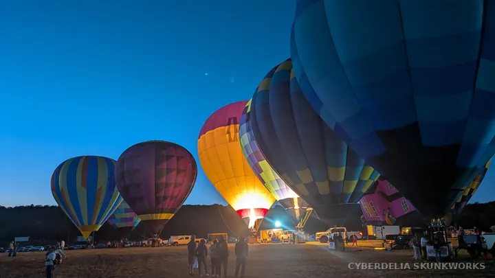 Balloon envelopes tower over vehicles as the glow begins.