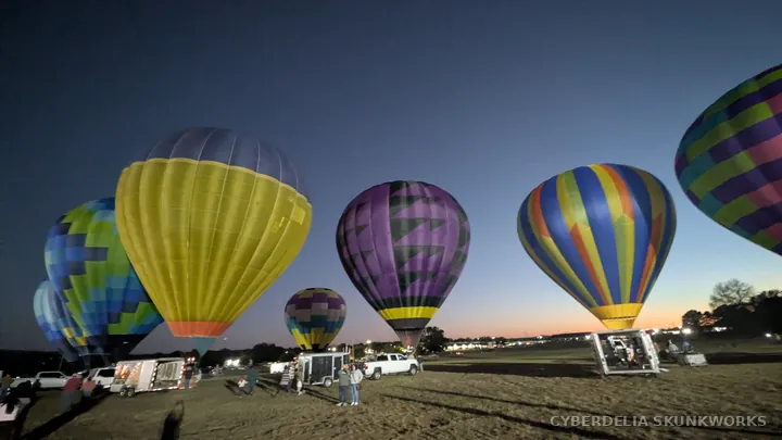 A wide view of balloons, support vehicles and the night sky.