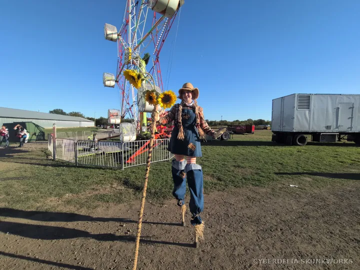 A scarecrow-style stilt walker from Inspyral Circus carries sunflowers.