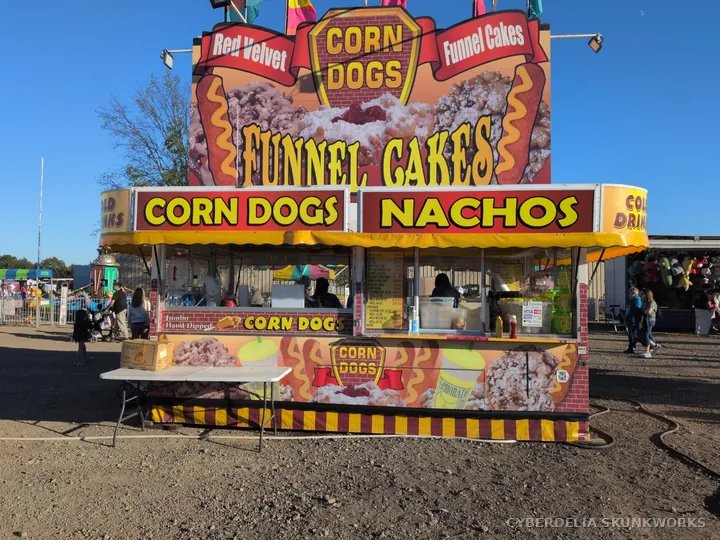 A food stand advertises corn dogs, funnel cakes and nachos.