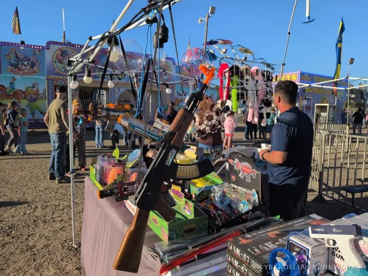 A vendor displays colorful merchandise beside the midway.