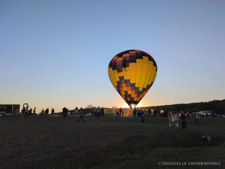 A yellow-and-checkered balloon rises above the field at sunset.