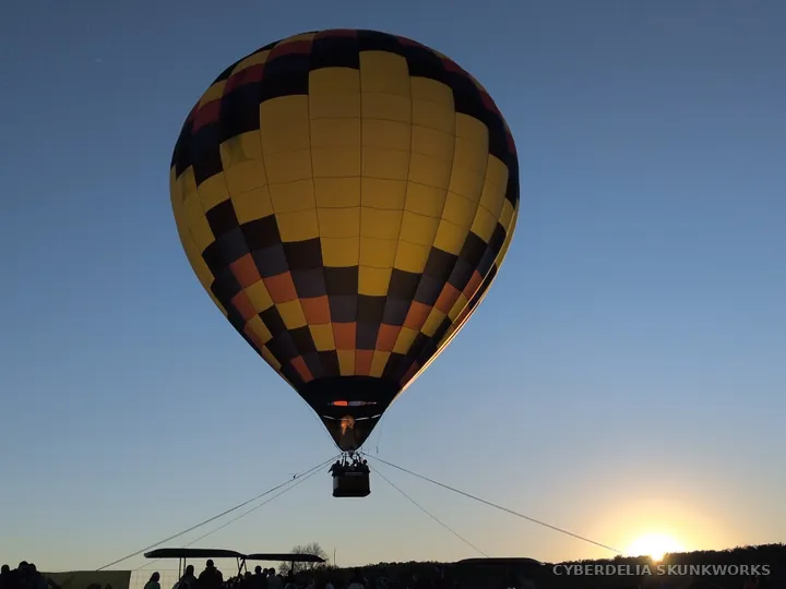 A tethered balloon is silhouetted against the setting sun.