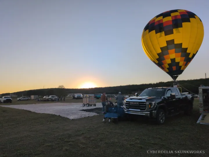 A balloon and support vehicles share the evening field.