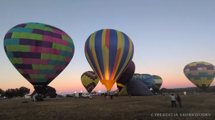 A burner fires beneath a striped balloon across the open field.